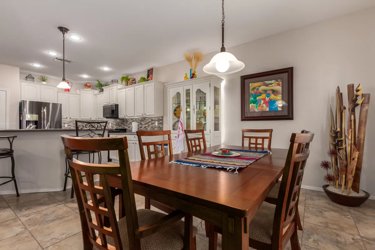 Open-plan view of a dining area adjacent to the kitchen, featuring a dining table with a colorful runner, modern appliances in the background, and thoughtfully curated decorative elements. The space feels lively and perfect for both family meals and entertaining friends.