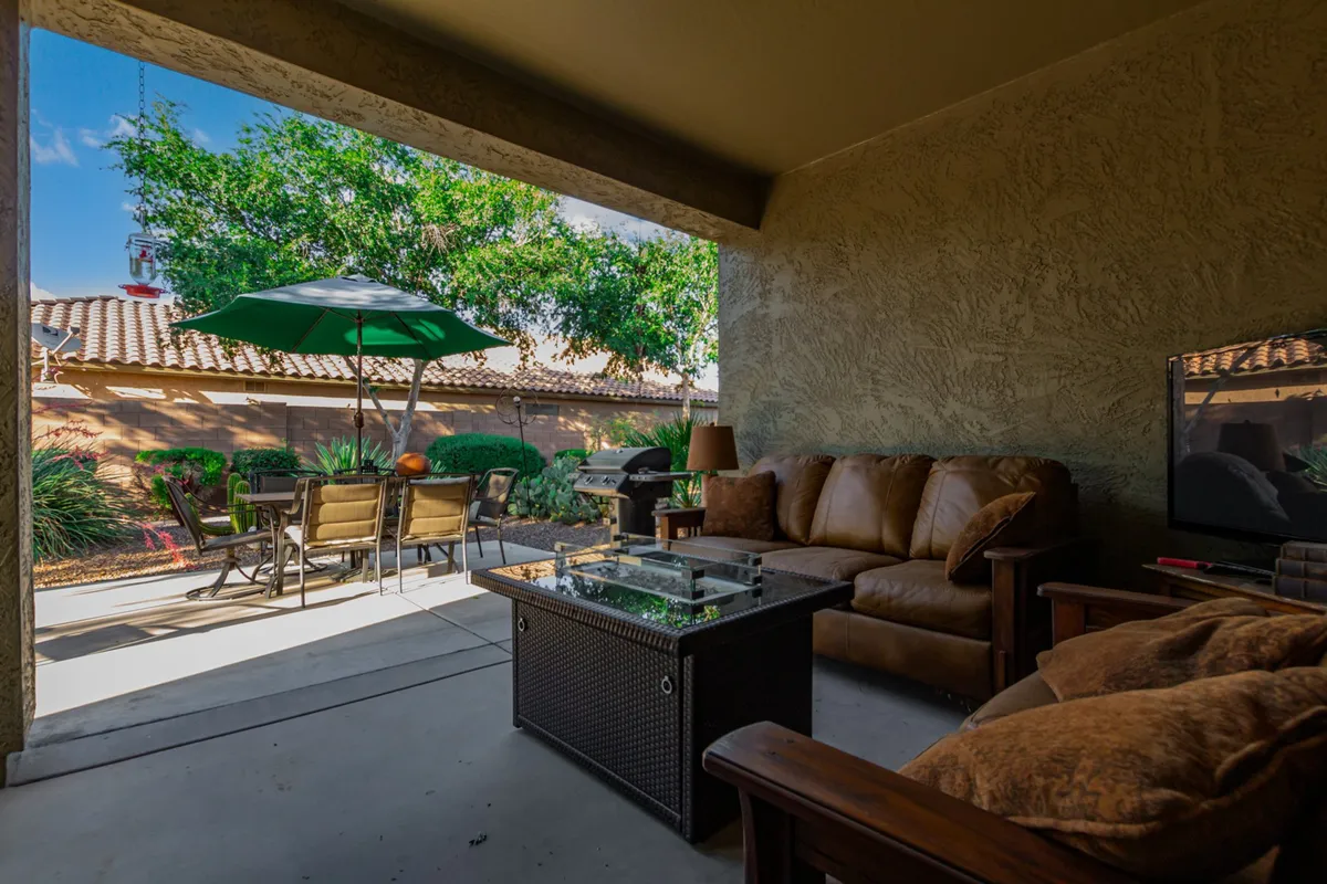 A casual outdoor seating area with green umbrellas, a patio table, BBQ grill, and lush greenery all around. The space is designed for both relaxation and entertaining, with a welcoming atmosphere accentuated by the vibrant garden and amenities.