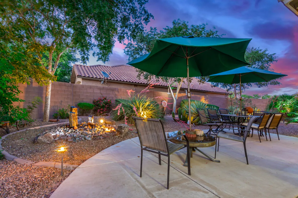 A cozy exterior seating area with green umbrellas, a fire pit, and a landscaped garden. The space is inviting for relaxation or informal gatherings, with a tranquil mood suited to both unwinding after work and casual business chats outdoors.