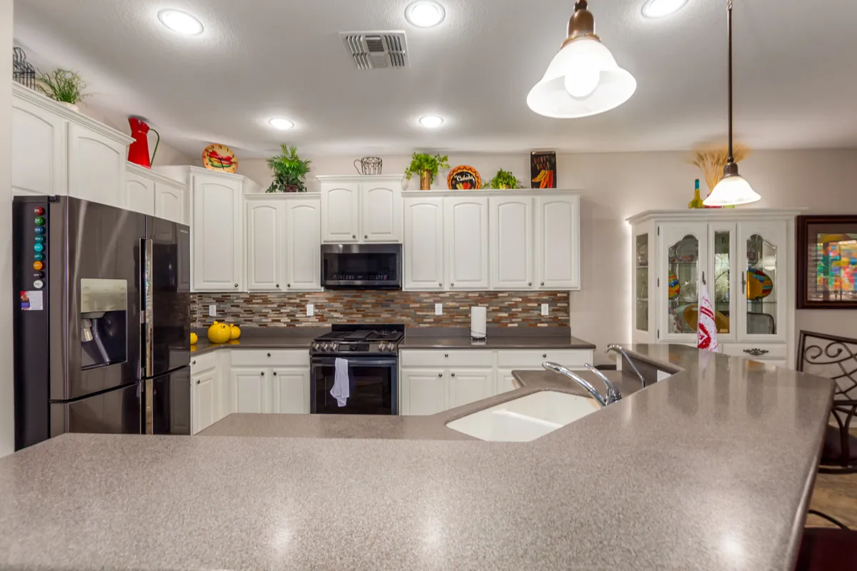 A bright, cheerful kitchen interior with a prominent island, stainless steel appliances, decorative plants, and colorful dishes on display. The setup emphasizes ample counter space for preparing meals and socializing, reflecting a lively and functional environment.