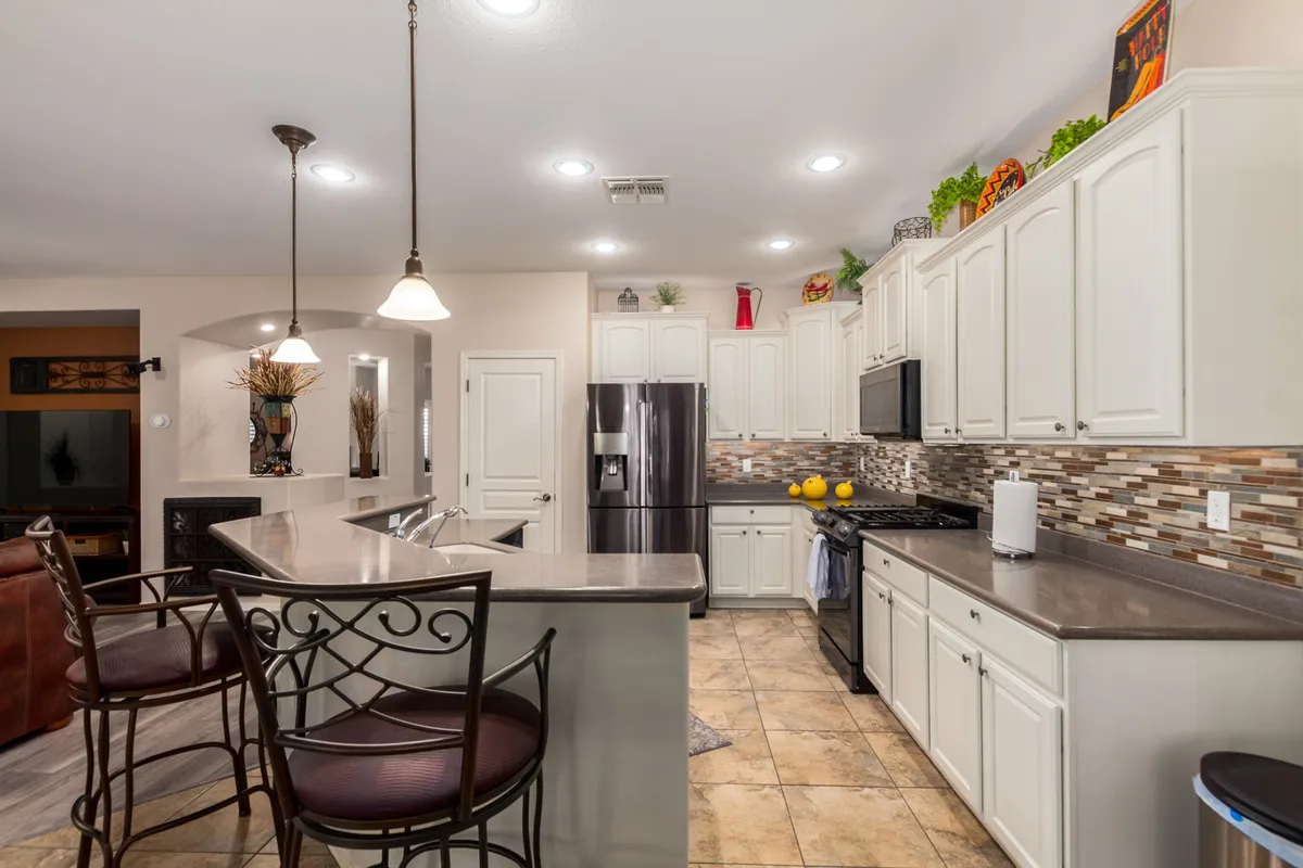A warmly lit kitchen featuring a central island with bar stools, modern appliances, and eye-catching backsplash tiles. The scene exudes a welcoming mood, ideal for hosting dinner parties or casual brunches.