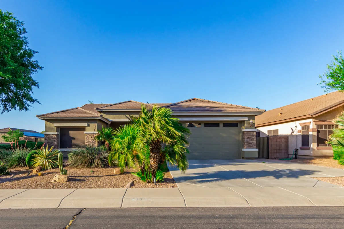 This image shows the home's front yard landscaping, a clear view of the garage door, and palm trees lining the property. The driveway leads to the three-car garage, and the overall setting is inviting, with lush plantings and ample natural light suggesting a comfortable and secure entry.