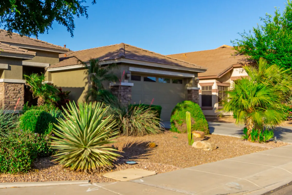 This image features a neatly landscaped front yard with palm trees, a visible garage door, and a tidy pathway leading to the home's main entrance. The welcoming exterior hints at ample storage and curb appeal, ideal for long-term renters seeking ease and convenience.